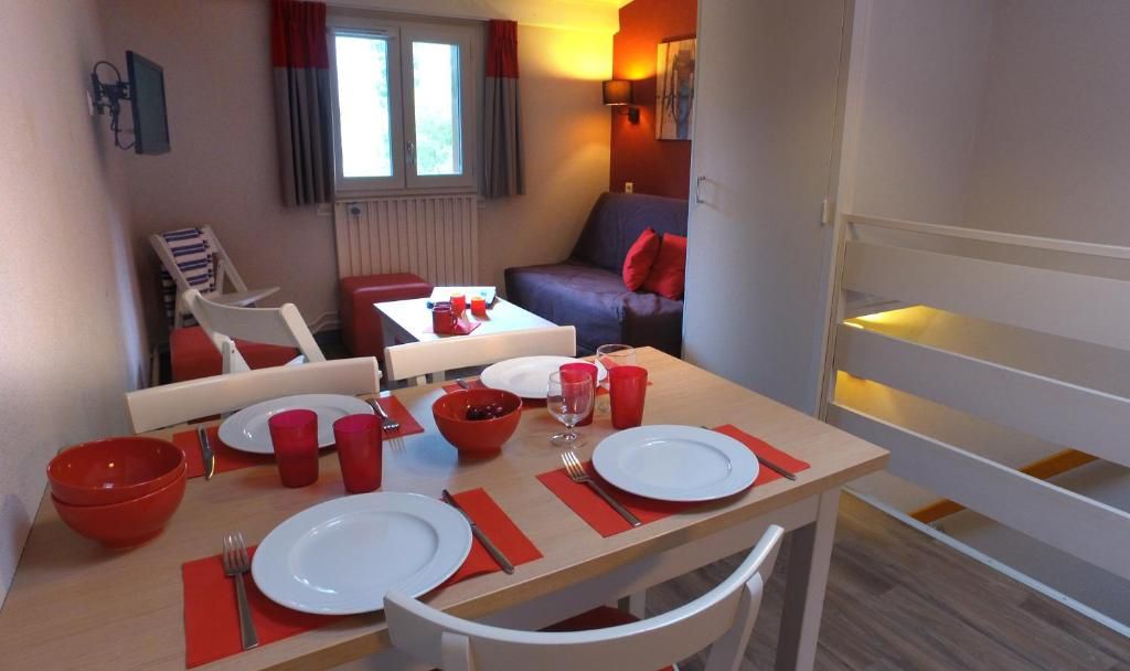 Un coin repas avec une table dressée pour quatre personnes, comprenant de la vaisselle rouge et blanche, un bol et un verre à vin.