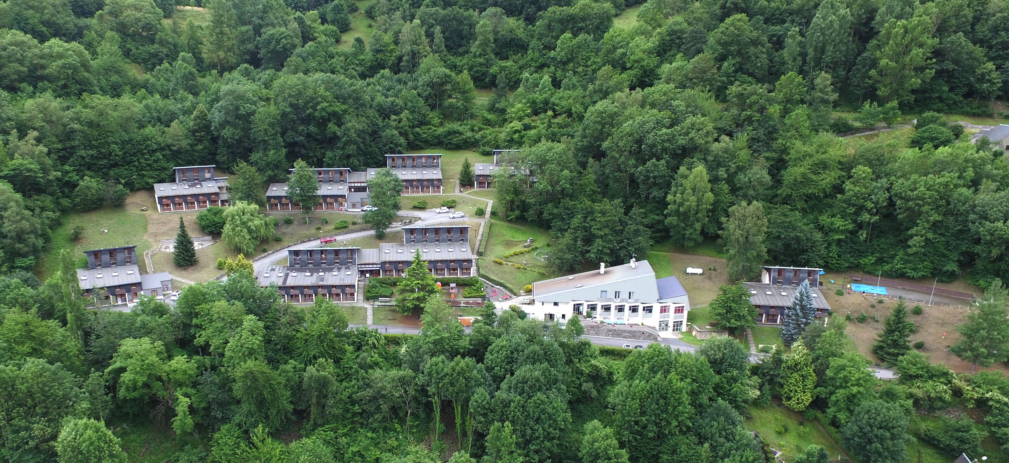 Un conjunto de edificios rodeado de un bosque denso, con varias áreas de estacionamiento y un edificio central con un techo grande.