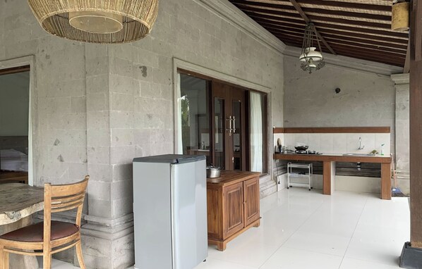 A kitchen with a refrigerator, wooden cabinets, a dining table with chairs, and a hanging light fixture.