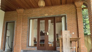 A brick building with a wooden door, a number '21' sign, and a small table outside. - Bagiya Suites & Villas by Zuzu (Sebatu)