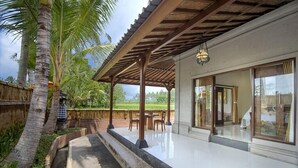 A covered outdoor area with a pool, palm trees, and a building with large windows. - Bagiya Suites & Villas by Zuzu (Sebatu)