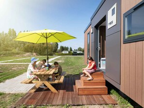 Ein modernes Gebäude mit einer Holzterrasse, einem Picknicktisch und einem gelben Sonnenschirm.
