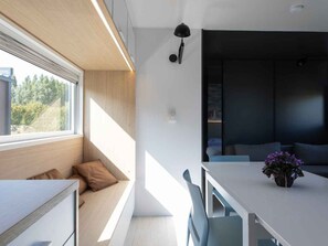 Ein modernes Interieur mit Essbereich, einer eingebauten Bank mit Kissen, einem weißen Tisch und einer Topfpflanze.