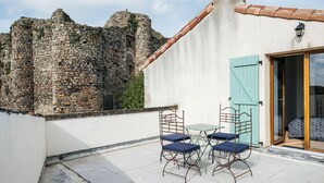 Een terras op het dak met stenen muren, een betegelde vloer en een tafel met stoelen.