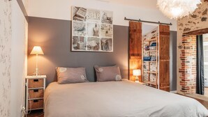 A bedroom with a bed, two bedside lamps, a wall-mounted picture, a wooden wardrobe, and a brick wall. - Gorgeous home in Sevremont with WiFi (Sevremont)