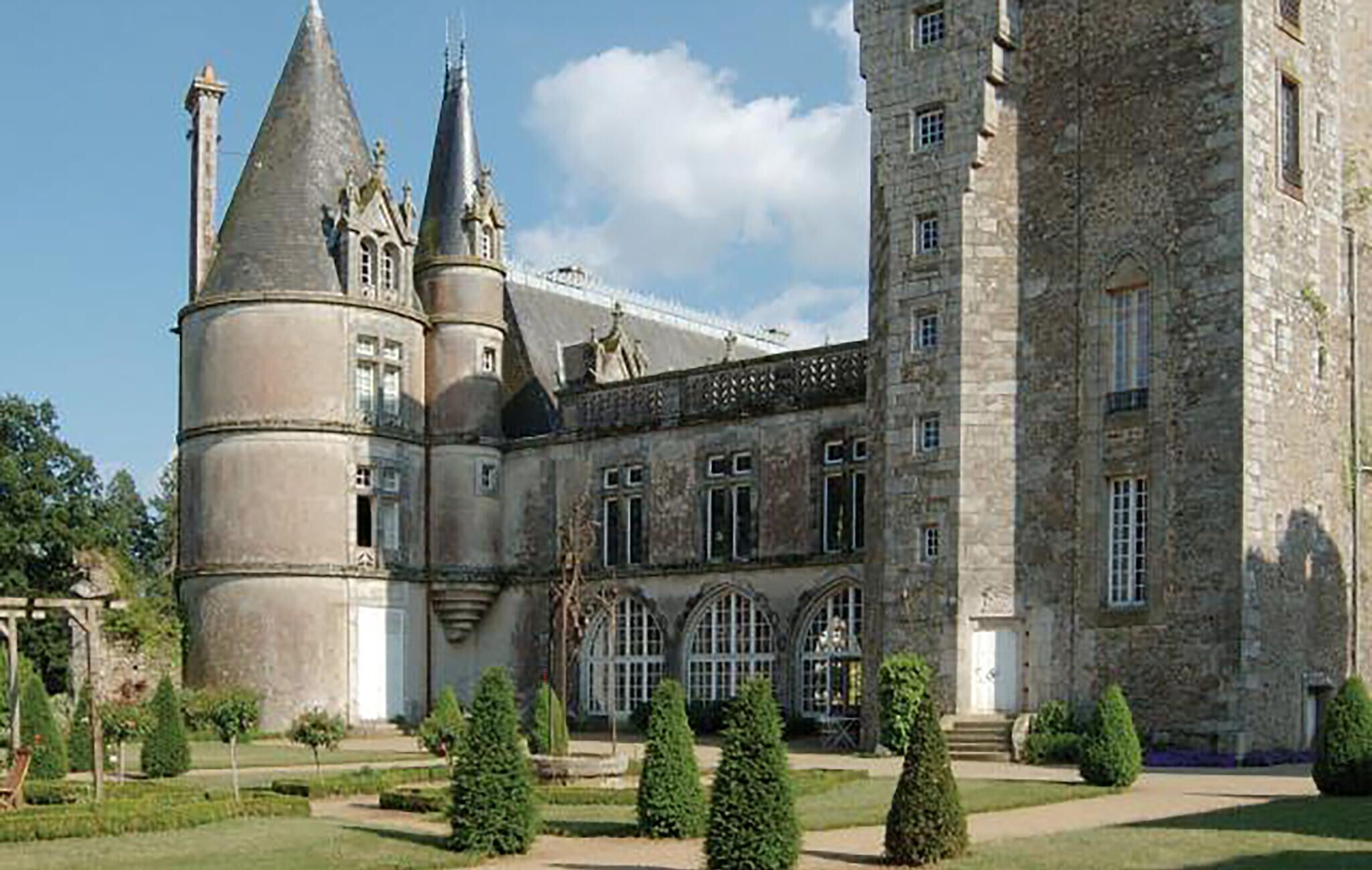 A large, historic building with multiple towers and a well-maintained garden.
