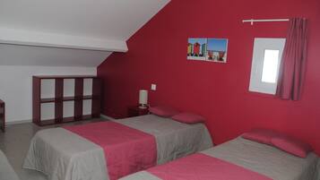 Une chambre avec deux lits, un mur rouge, une fenêtre avec des rideaux et une petite table avec une lampe.