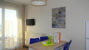 A small dining area with a table, chairs, a television mounted on the wall, and a painting.