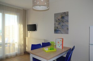 A small dining area with a table, chairs, a television mounted on the wall, and a painting. - Vvf Villages Saint-cast-le-guildo (Saint-Cast-le-Guildo)