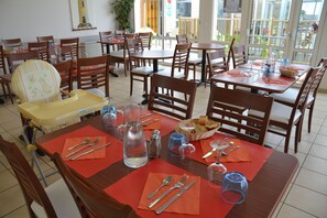 A dining area with multiple tables and chairs, some with red placemats and cutlery. - Vvf Villages Saint-cast-le-guildo (Saint-Cast-le-Guildo)