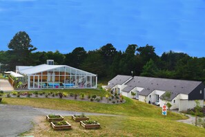 A modern building with a glass facade, surrounded by a landscaped garden and residential houses. - Vvf Villages Saint-cast-le-guildo (Saint-Cast-le-Guildo)