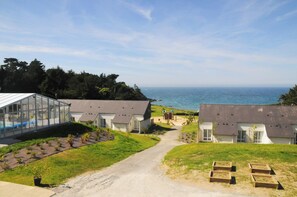 A coastal property with a glass greenhouse, white houses, and a dirt path leading to the sea. - Vvf Villages Saint-cast-le-guildo (Saint-Cast-le-Guildo)