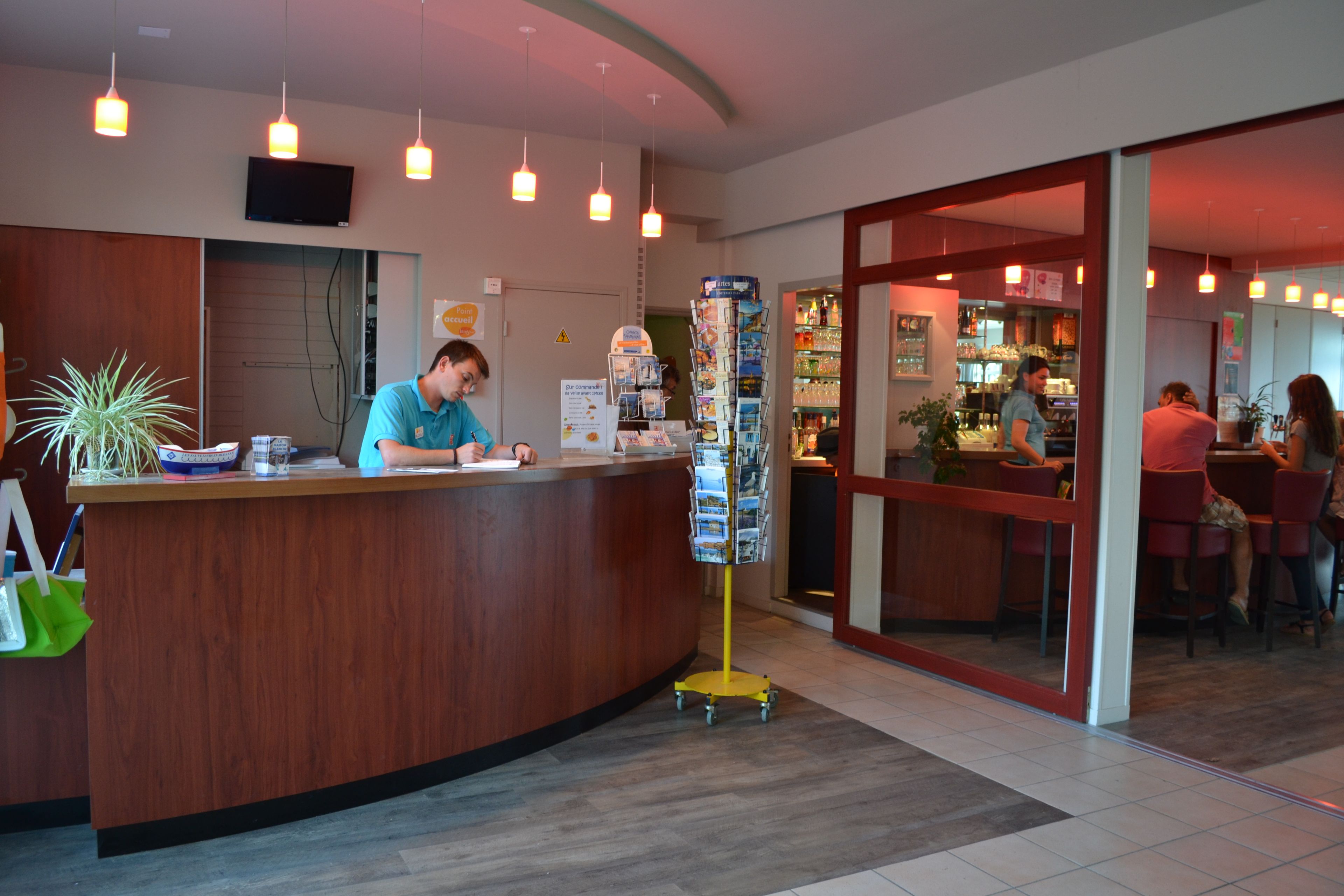 Een receptiebalie van hout, een aan de muur bevestigde televisie en een plant aan de linkerkant.