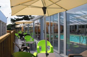 A poolside area with glass-enclosed seating and umbrellas. - Vvf Villages Saint-cast-le-guildo (Saint-Cast-le-Guildo)