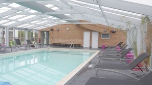 Una piscina con lettini, un muro in legno e un soffitto con finestra a lucernario.