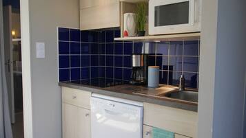 A compact kitchen with a dishwasher, a coffee maker, and a microwave on the countertop.