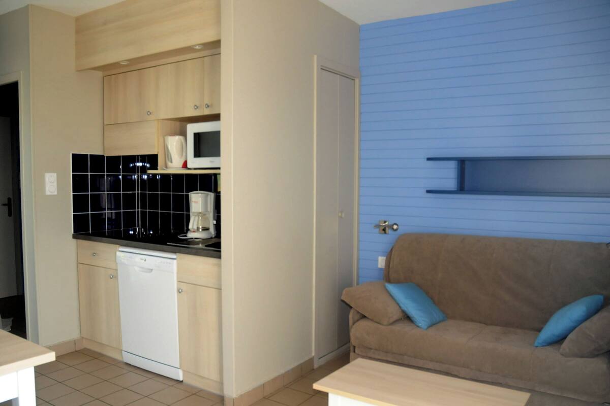 Un espacio habitable compacto con kitchenette, un sofá y una pequeña mesa.