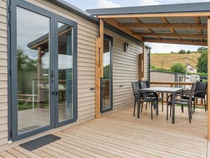 Eine überdachte Terrasse mit Tisch und Stühlen, eine Glasschiebetür und ein Holzboden.