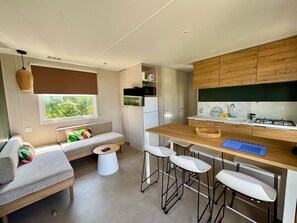 Eine kompakte Küche mit Holzarbeitsplatte, Barhocker, eingebautem Backofen und einem Fenster mit Blick ins Grüne.