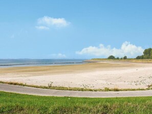 Eine Küstenstraße führt zu einem Sandstrand, der bewölktem Himmel entgegenführt.