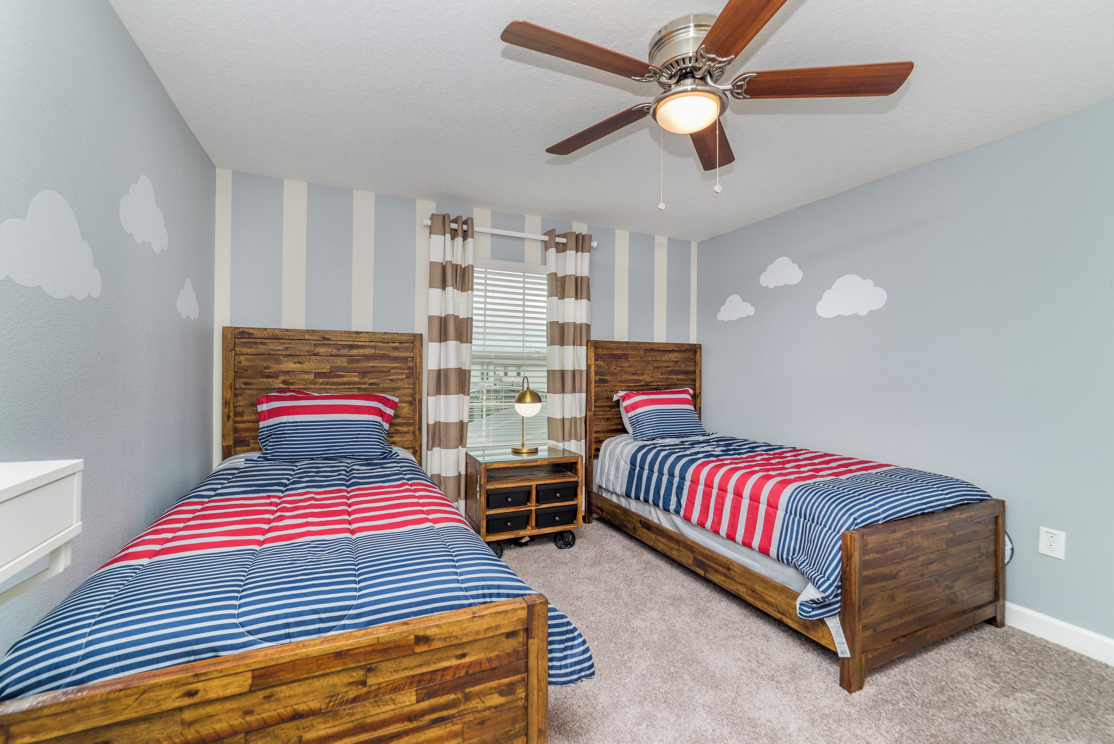 A bedroom with two wooden beds, a ceiling fan, and striped bedding.