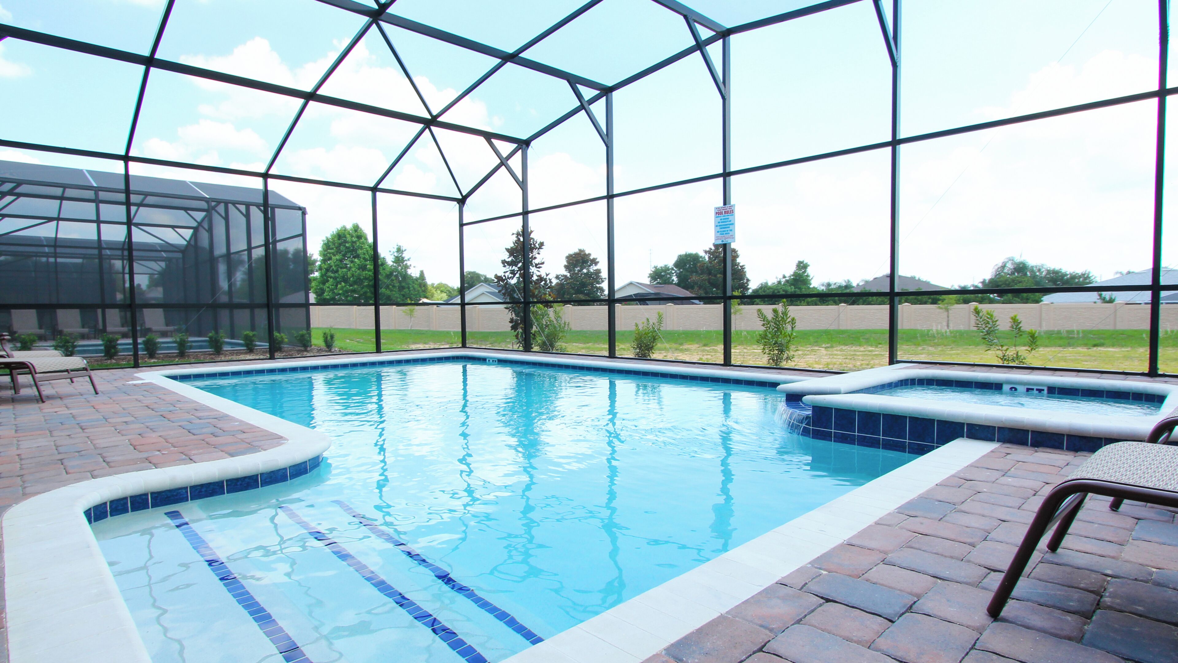 A swimming pool with a glass enclosure, a hot tub, and a patio area with chairs.