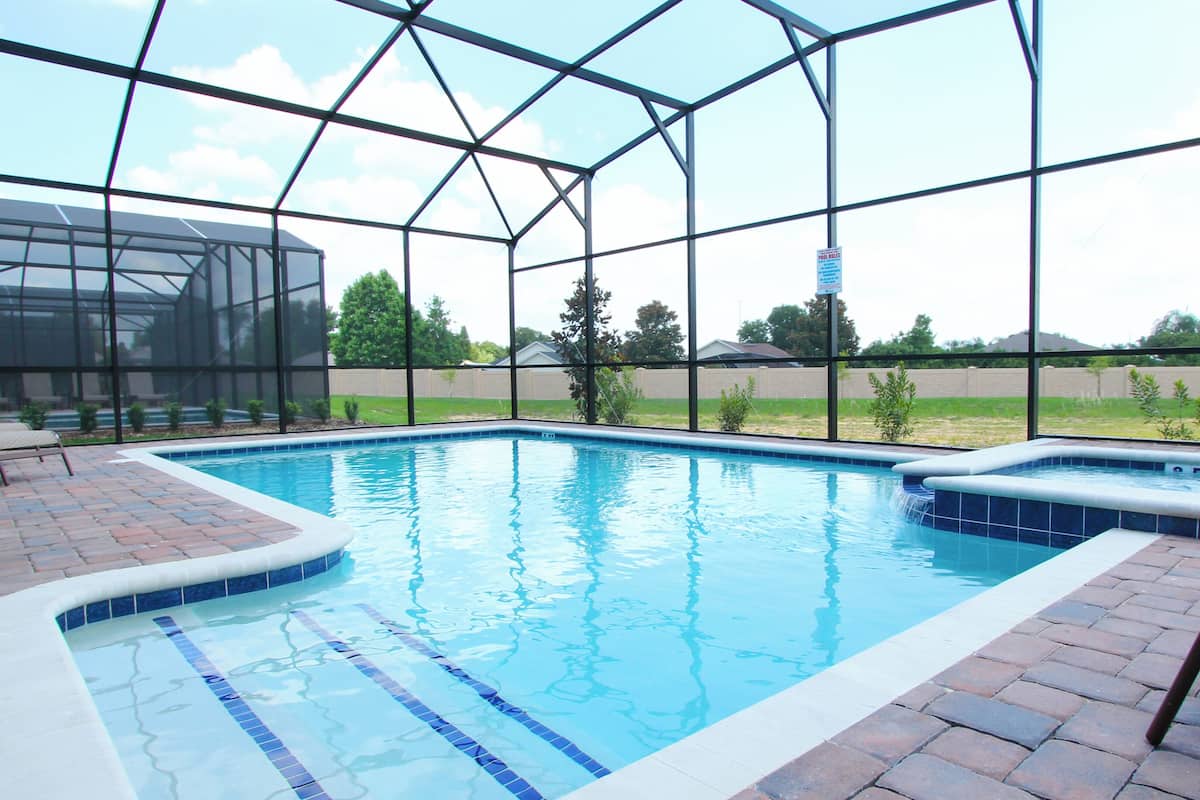 Ein Schwimmbad mit Glasveranda, ein Whirlpool und eine Terrassenfläche mit Stühlen.
