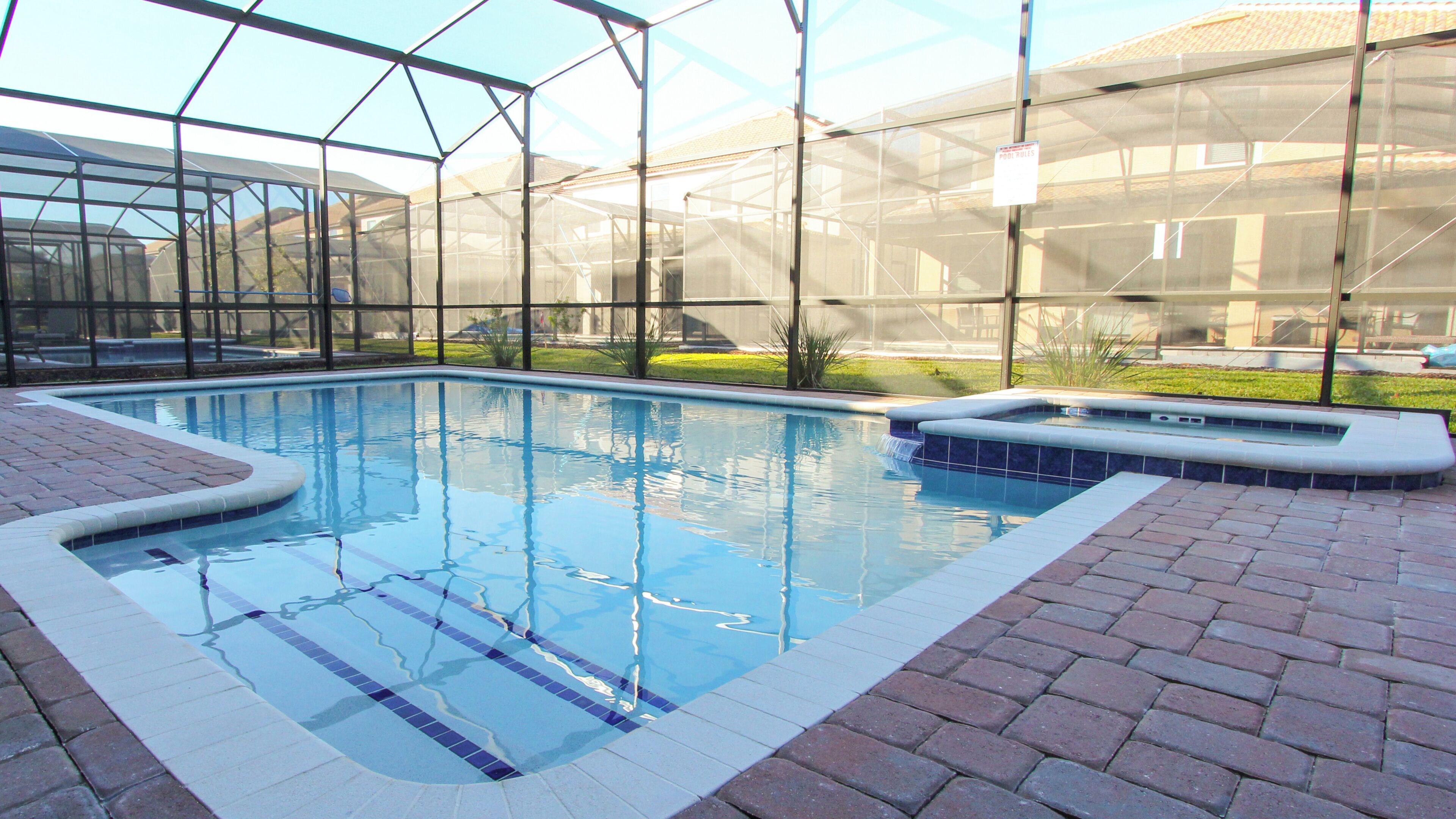 A swimming pool with a glass enclosure, surrounded by brick walkways.