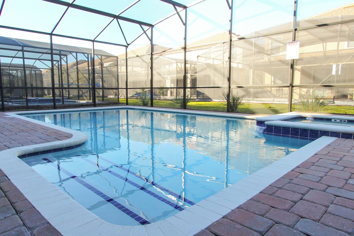 Ein Schwimmbecken mit Glasüberdachung, umgeben von Pflasterwegen.