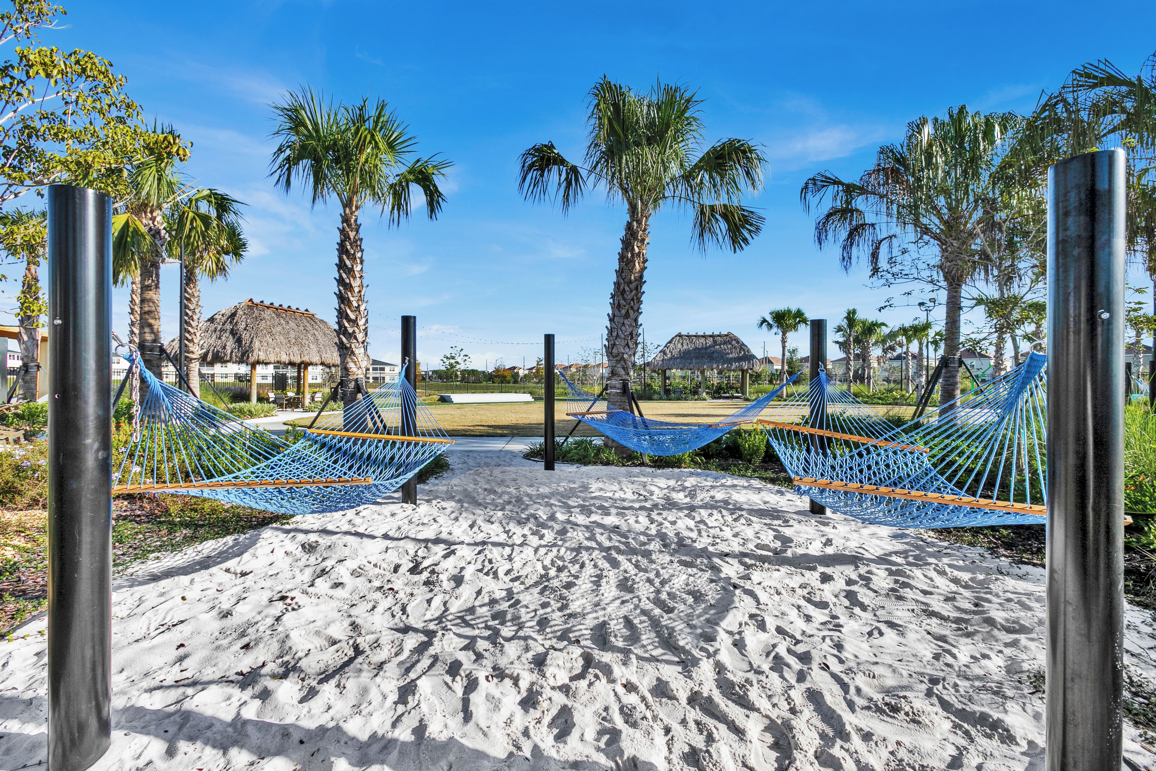 A beach with hammocks, palm trees, and a thatched-roof structure.