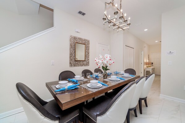 Un comedor con una mesa de madera dispuesta para seis personas, rodeada de sillas negras y blancas, un candelabro y un espejo decorativo en la pared.