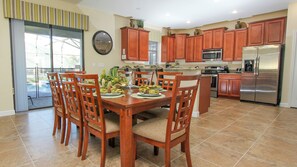 A dining area with a wooden table and chairs, a kitchen with wooden cabinets and stainless steel appliances, and a large window with a view. - Championsgate Resort Homes and Townhomes (Davenport)