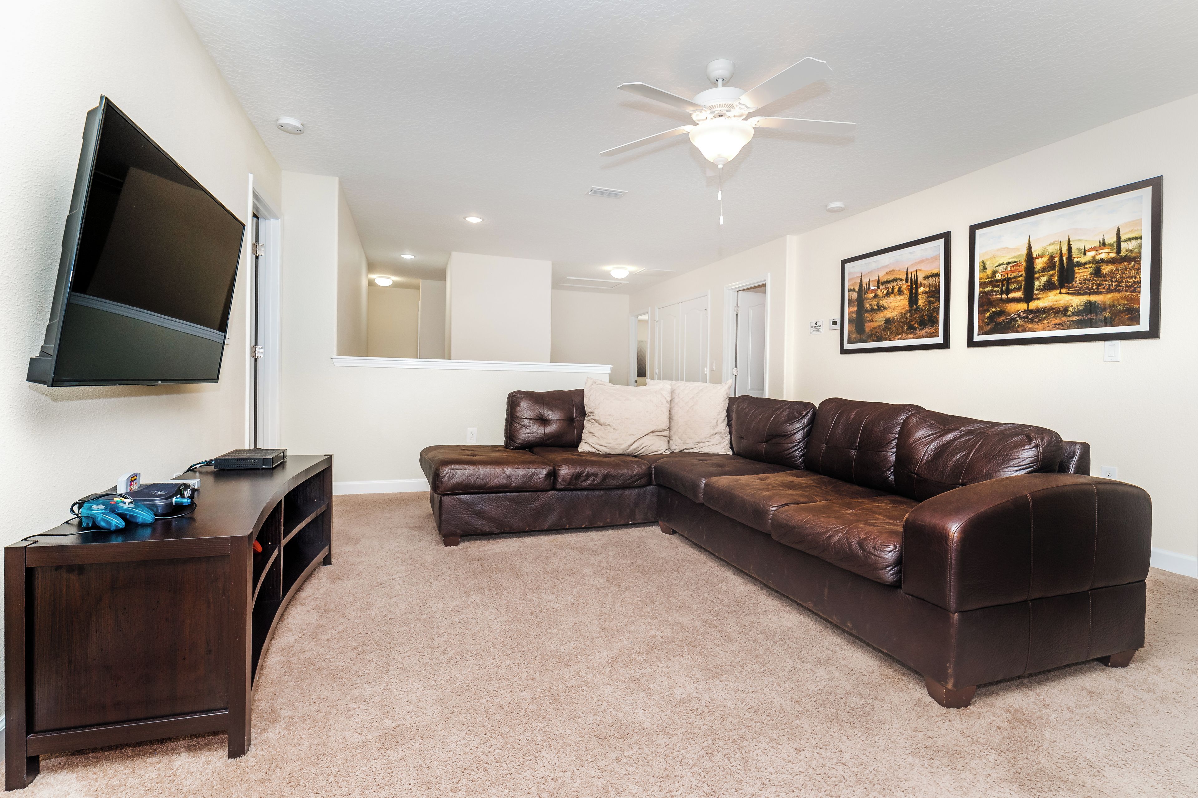 A living room with a sectional sofa, a TV mounted on the wall, and a ceiling fan.