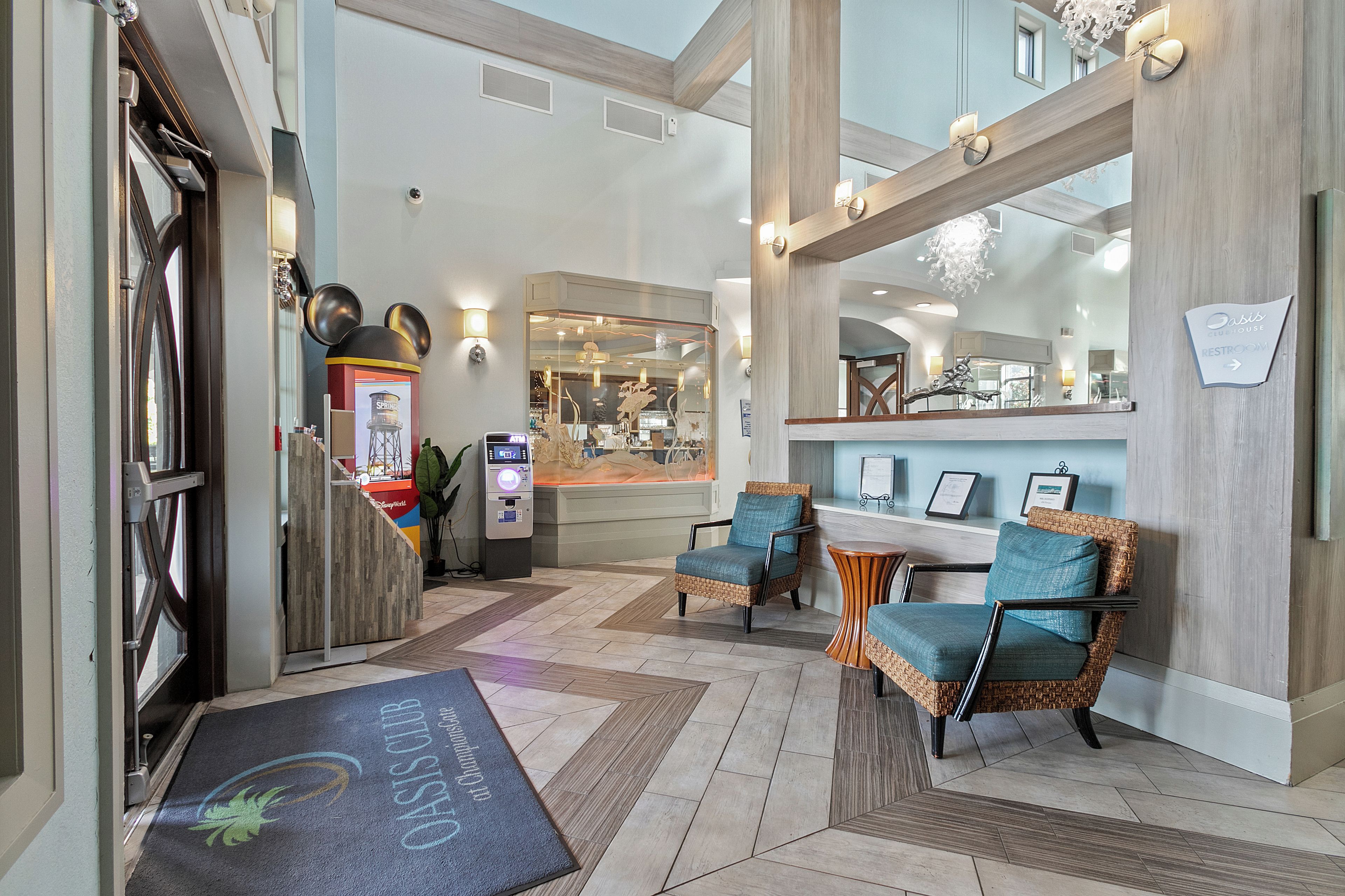 A lobby with a reception desk, two wicker chairs with cushions, a large mirror, and a reception area.