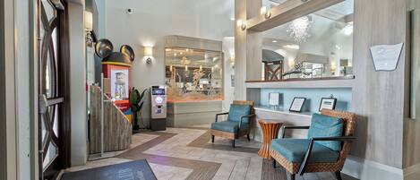 A lobby with a reception desk, two wicker chairs with cushions, a large mirror, and a reception area.