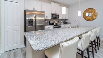 A kitchen with white cabinets, stainless steel appliances, a granite countertop, and bar stools.