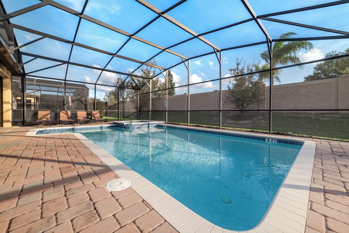 Ein Schwimmbecken mit Glasveranda, umgeben von Ziegelböden und einer überdachten Terrasse.
