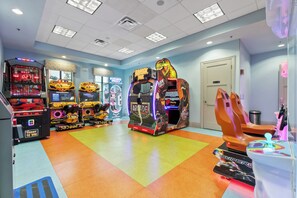 Eine Indoor-Spielhalle mit verschiedenen Spielautomaten, darunter eine mit Dinosaurier-Motive, und ein hell erleuchteter Raum mit einem farbenfrohen Boden.