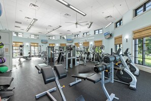 Une salle de sport équipée de divers appareils d’exercice, dotée de grandes fenêtres et d’un ventilateur de plafond.