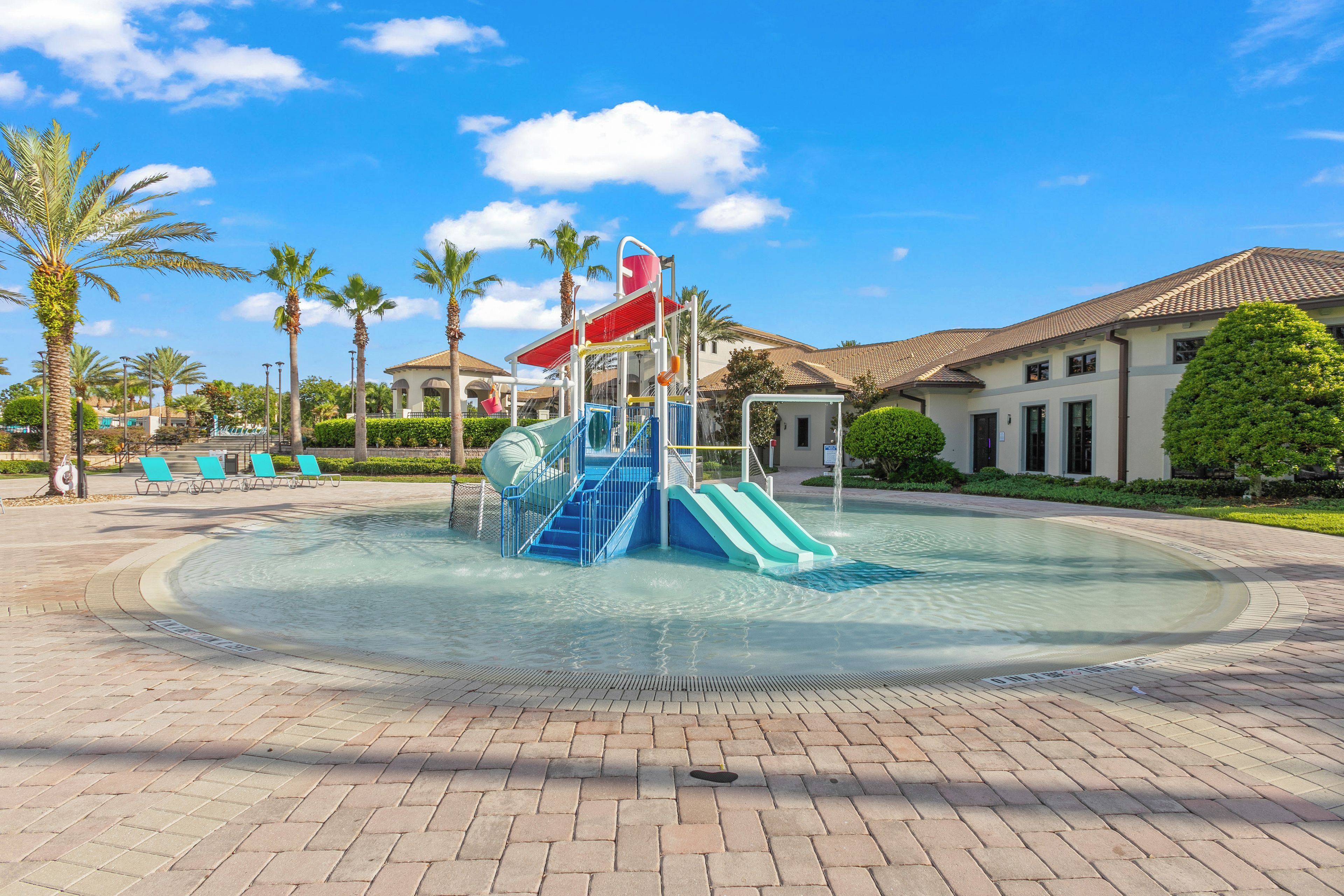 A swimming pool with a water slide, palm trees, and a building in the background.