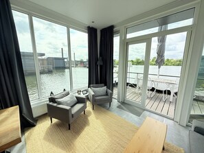 Ein modernes Zimmer mit großen Fenstern, einem Sofa, einem kleinen Tisch und Blick auf ein Gewässer.