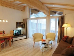 Ein Wohnzimmer mit Holzbalkendecke, einem Fernseher, einem Sofa und einem Couchtisch.