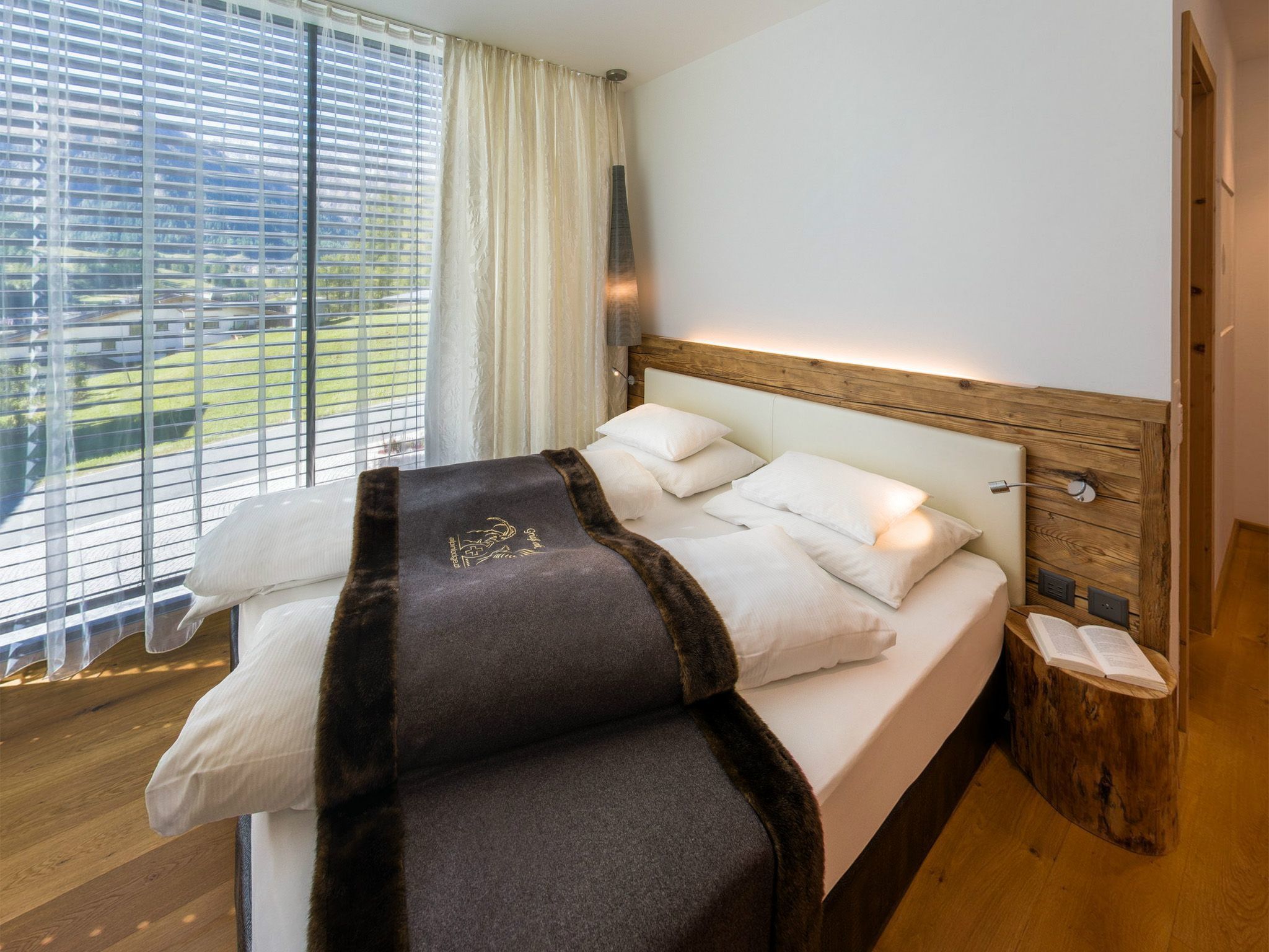 Un dormitorio moderno con una cama grande, cabecera de madera y vista a un paisaje verde a través de la ventana.