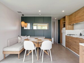 Eine moderne Küche mit Holzausstattung, einem Essbereich mit rundem Tisch und weißen Stühlen sowie einer integrierten Bank mit Kissen.