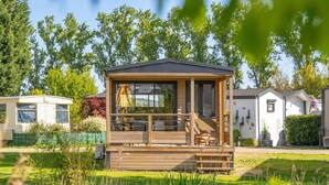 Une cabane en bois dotée d’un balcon, entourée de verdure et bordée d’un étang.
