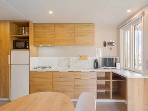Eine moderne Küche mit Holzausbau, einer weißen Arbeitsplatte, einer eingebauten Mikrowelle, einem Gasherd und einem Fenster mit Jalousien.