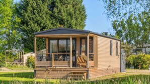 Une cabane en bois dotée d’un porche abrité, d’une petite terrasse et offrant une vue sur un étang.