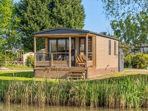 Eine Holzblockhütte mit überdachter Veranda, einer kleinen Terrasse und Blick auf einen Teich.