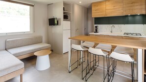Cocina compacta con encimera de madera, microondas integrado y cocina a gas. Cuenta con una zona de estar con sofá y una pequeña mesa redonda.