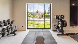 Un gimnasio con un amplio ventanal, estantes para pesas y vistas a un edificio cercano.